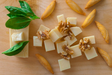 Closeup of pieces of cheese, toast, walnuts and basil leaves on wood.
