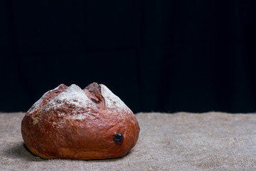 Still-life with fresh bread on sackcloth on black background, with space for text, selective focus