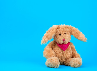 Cute plush beige rabbit with a pink tie sits on a blue background