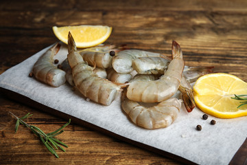 Fresh raw shrimps with lemon and rosemary on wooden table, closeup