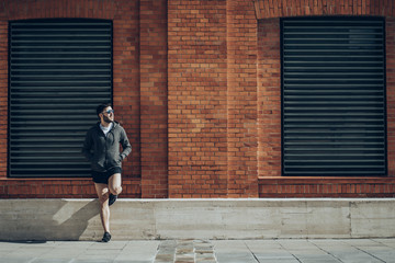 Man with sport clothes looking away while is supporting on an orange bricks wall