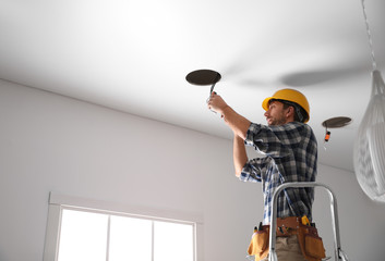 Worker installing lamp on stretch ceiling indoors. Space for text