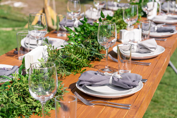 Beautifully decorated wooden table in a summer open-air cafe. Green branch and fresh flowers table decoration