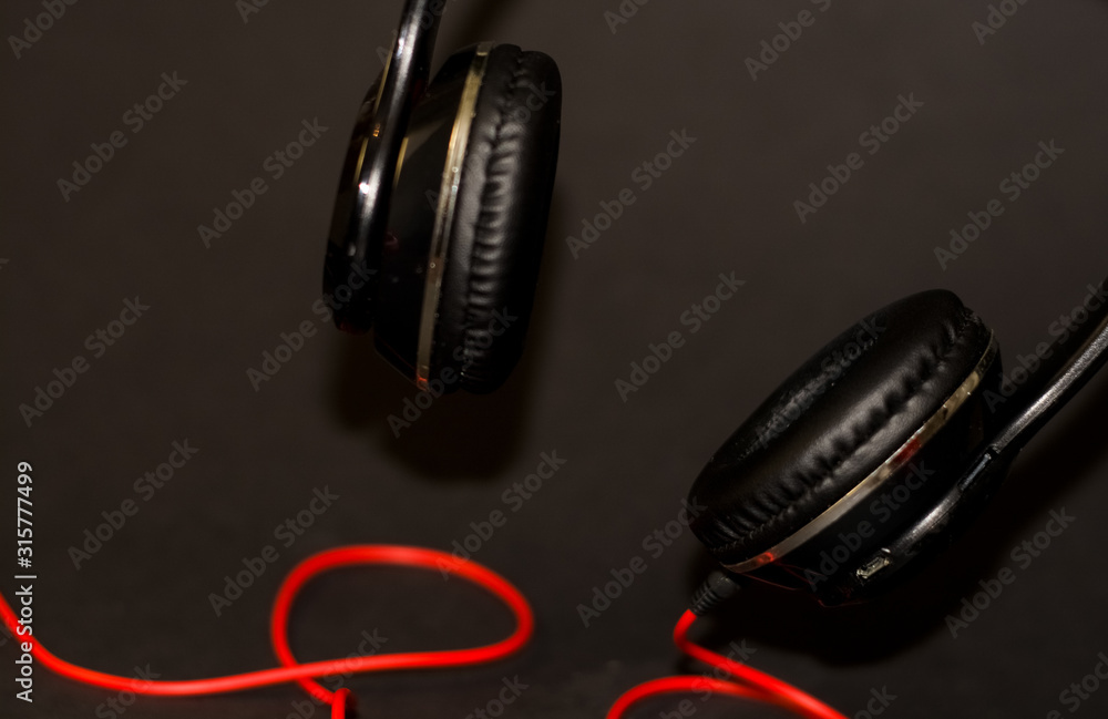 Wall mural on black background, large headphones for listening to music with red elements and cord.