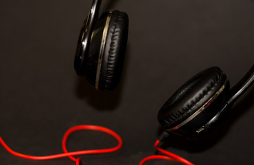 On black background, large headphones for listening to music with red elements and cord. 