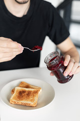 The guy has breakfast with toast with jam.