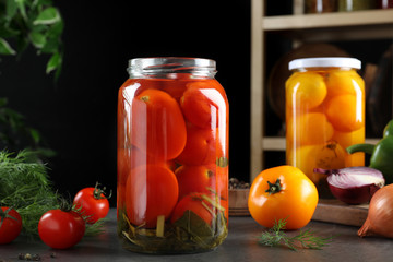 Glass jars of pickled tomatoes on grey table