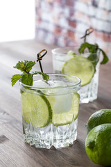 A close up of a glass of sparkling water with lime and another one in behind on a wooden table against a sunny window.