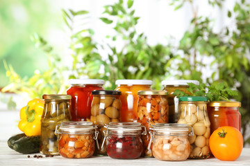 Glass jars of different pickled vegetables on white wooden table