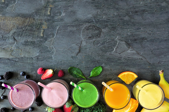 Assorted healthy fruit smoothies in. Top view bottom border against a dark background. Copy space.