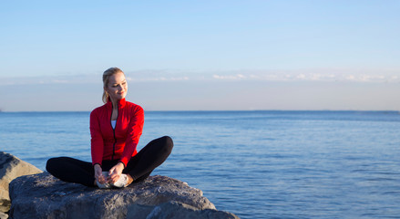 young blonde woman in sport dress is doing exercise sitting at seaside