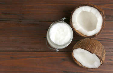 Halves of ripe coconut and organic oil on wooden table, flat lay with space for text. Healthy cooking