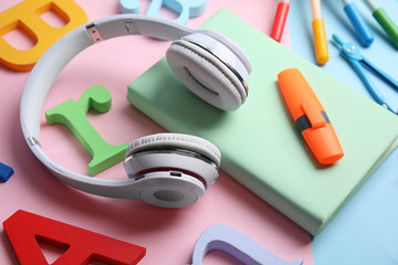 Book, headphones and stationery on color background