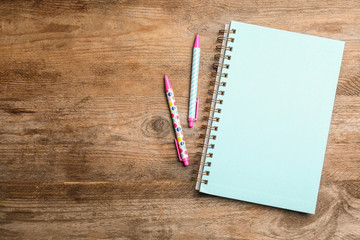 Stylish notebook and pens on wooden table, flat lay. Space for text