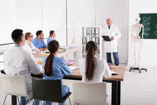 Medical students and professor studying human skeleton anatomy in classroom