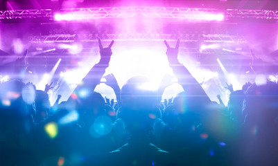 Image shot during a music festival. Light comes from a stage with a band show, people silhouettes...