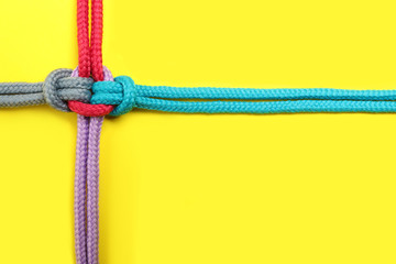 Top view of colorful ropes tied together on yellow background, space for text. Unity concept