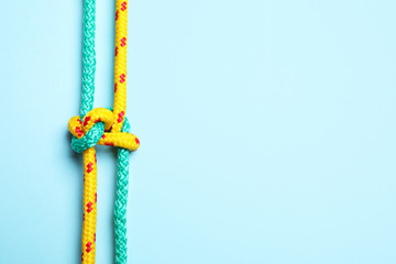 Top view of colorful ropes tied with knot on light blue background, space for text. Unity concept