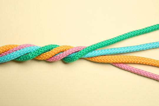 Twisted colorful ropes on beige background, top view. Unity concept