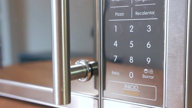 Extreme close-up of hand pressing time buttons on microwave oven with Spanish text, seen from the side