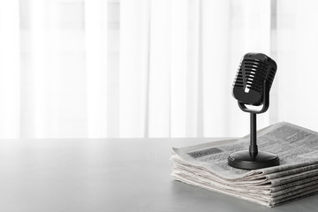 Newspapers and vintage microphone on grey table, space for text. Journalist's work