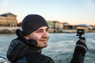 Happy frozen tourist shoots on an action camera of the Danube River surroundings in December.