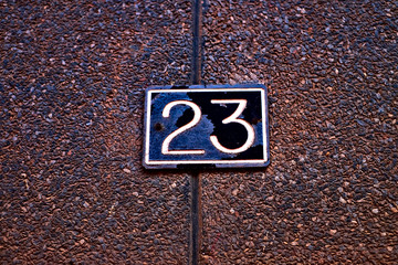 Number 23, twenty-three, white digits on a dark plate, dark brown dimpled background.