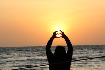 Woman making a heart with her hands in the sunset on te beach