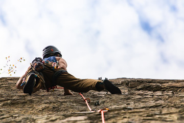 A low angle view of a rock climber in action, wearing kit belt with belay devices and safety...