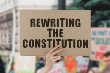 The phrase " Rewriting the constitution " on a banner in men's hand. Human holds a cardboard with an inscription. Government. Politics. Changing. Law. Lawyer. Policy. Rules. Country. State. Diplomacy