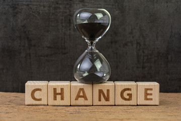 Change, transform or evolve to success in disruption world concept, sand glass or hourglass on cube block with alphabet building the word Change on wood table with dark black background