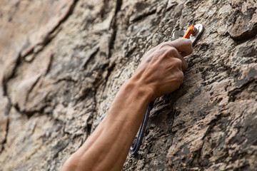 A close up view of advanced rock climbing gear in use as the hand of a man grabs onto a secured belay device, health and safety during risky sport - obrazy, fototapety, plakaty