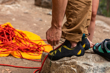 A closeup view on the hands and feet of a rock climber fastening laces of specialized climbing shoes, preparing to climb, with copy space to left