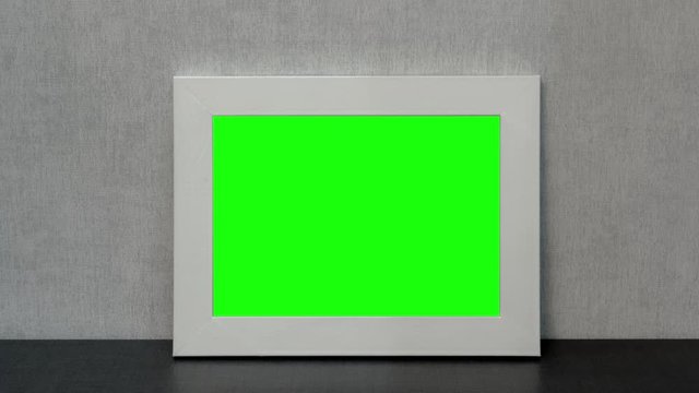 beautiful white photo frame with green chroma-key picture reflected on black table at grey wall close zoom in