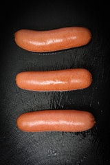 Three cooked sausages on a black basalt background