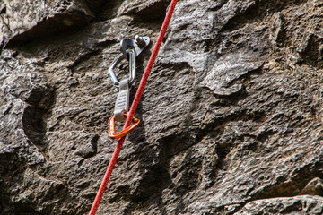 A close up and detailed view of a belay device and dynamic rope secured to a rugged limestone cliff. Professional rock climbing equipment in use - obrazy, fototapety, plakaty