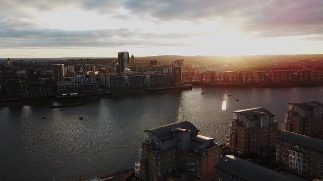 Drone flying over London's Thames river while a boat passes by under during sunset