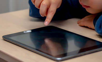 Close up front high view of a little boy's hand using and black tablet during the day time