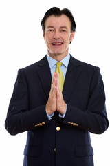 Studio shot of mature happy businessman smiling with hands clasped