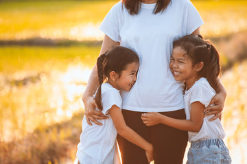 Two asian child girls hugging their mother and having fun to play with mother in the paddy field with the sunlight