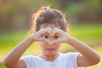 Cute asian child girl making heart shape with hands in the field with sunlight