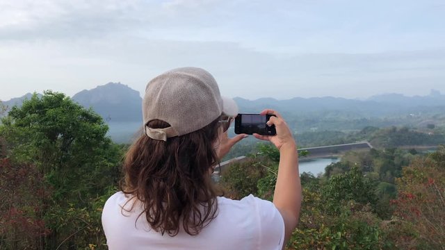 A woman travel blogger takes photos of Thailand's natural attractions on Lake Cheow Lan by phone, a close-up view of a woman from the back, she takes a photo for insagrams.