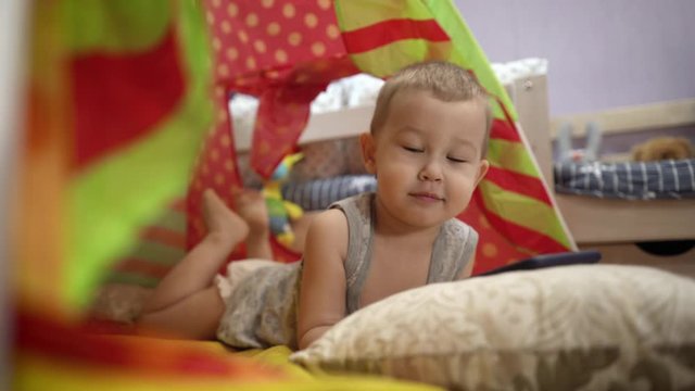 Charming baby plays with the phone in the children's tent. He watches videos and pictures.
