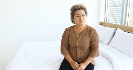 An elderly woman sitting alone on the bed.