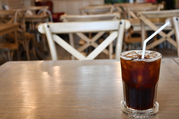 A glass of ice Americano on wooden table in cafe.