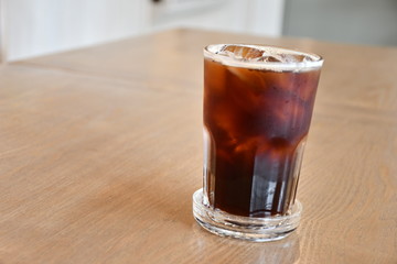 A glass of ice Americano on wooden table in cafe.