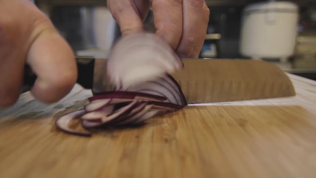 kitchen chef is cutting onions with a knife on wooden cut board in the restaurant