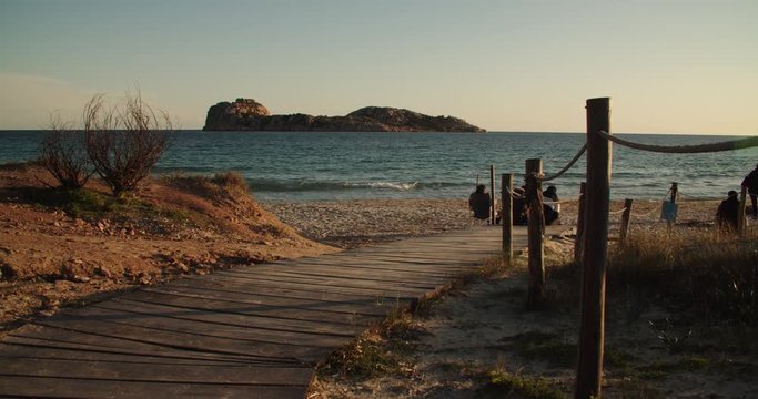 Wooden walkway at beach with people in front of island, sunset, Porto Tramatzu