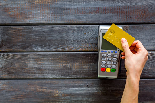 Contactless payment, paypass. Hand hold bank card near terminal on dark wooden background top-down copy space