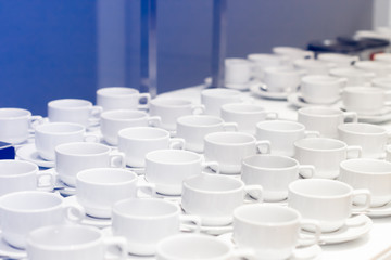 Many white coffee cups in a line over a buffet